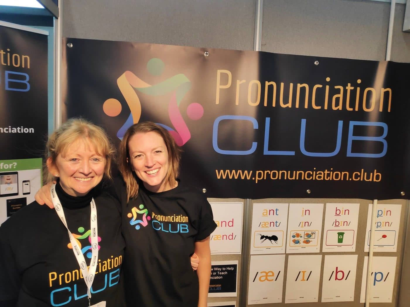Marianne and Tracy Quinn smiling in front of the Pronunciation Club banner